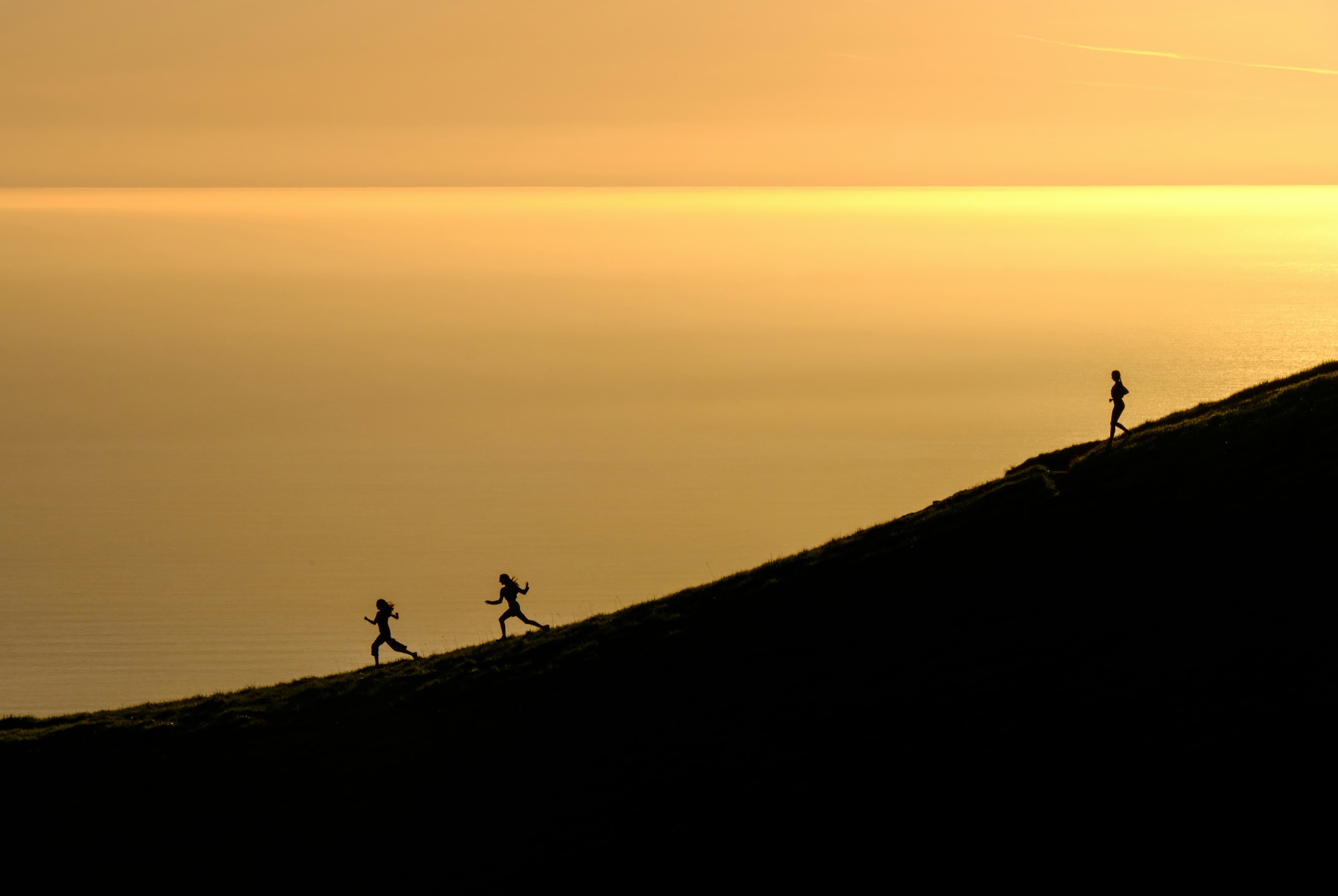 Runners silhouetted against golden ocean sunrise